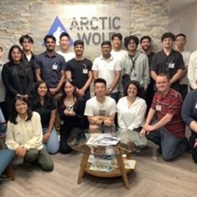 Group photo of Arctic Wolf employees and co-op students in front of the organization's logo in the office.