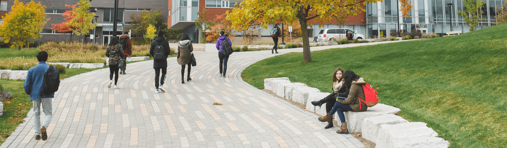 Two female students sitting on a low stone wall in front of the University of Waterloo Tatham Centre