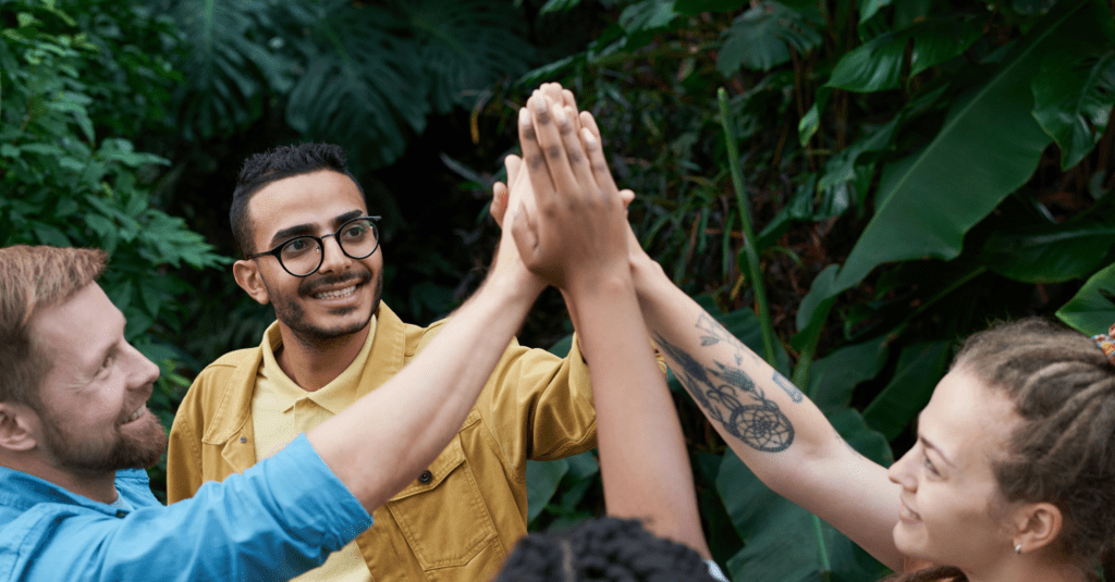 Four people high fiving outdoors.