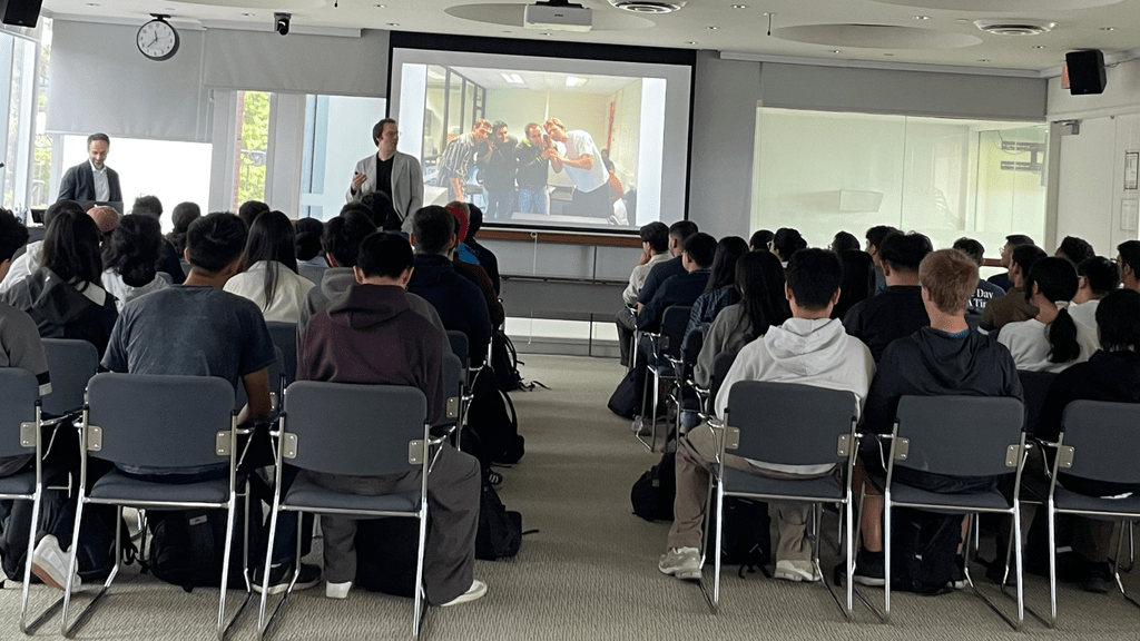 Students in an audience, two presenters and a slide show 