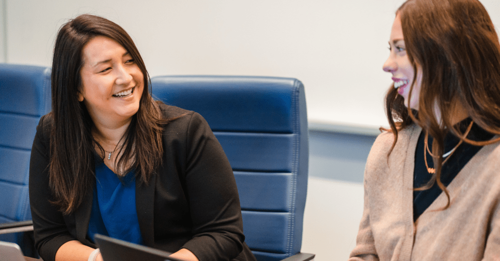 two women talking at a table with laptops