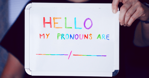 Person holding a small whiteboard that says "Hello my pronouns are" in multiple colours