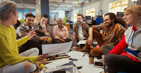 Diverse group of employees at a non-profit sitting in a group smiling, while looking at a project
