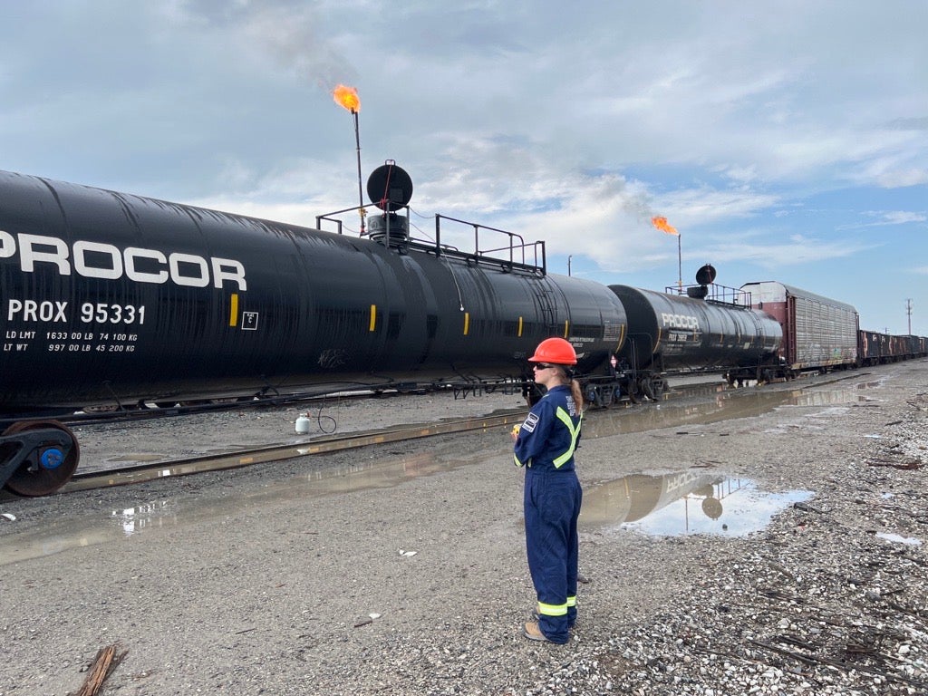 A female co-op student wearing a hard hat infront of a railcar during air monitoring.