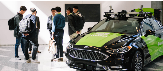Group of co-op students standing in a circle next to a NVIDIA green and black car.