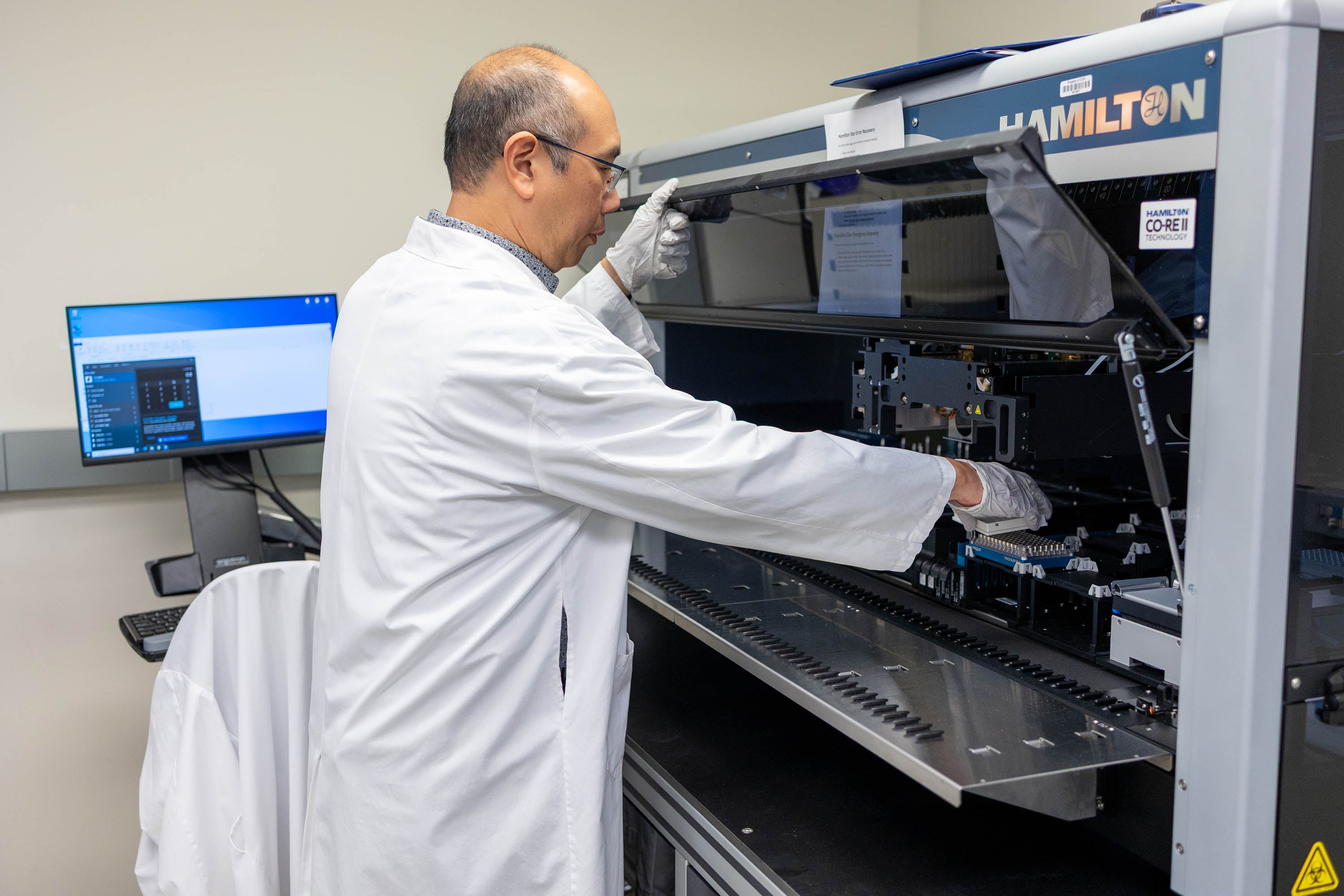Male team member at OICR looking into a machine to remove samples.
