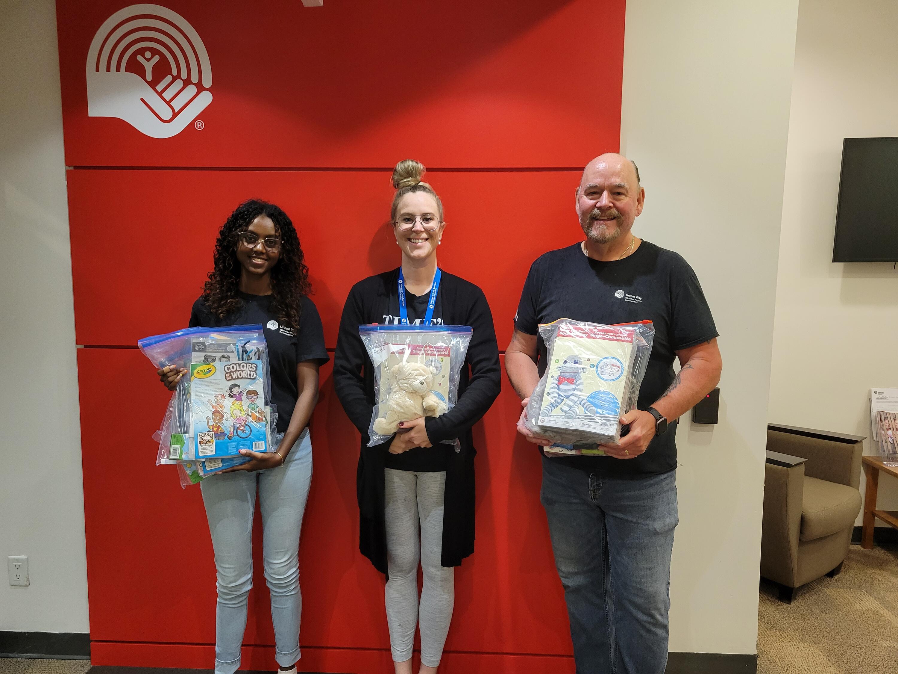 Three United Way employees and co-op students holding donation packages for kids
