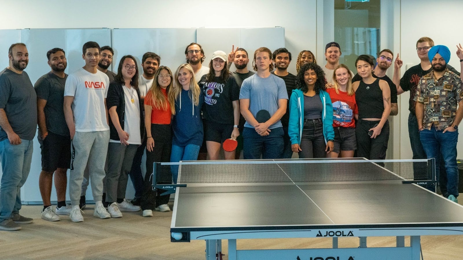 Perpetua employees and co-op students posing for a group photo in front of a ping pong table