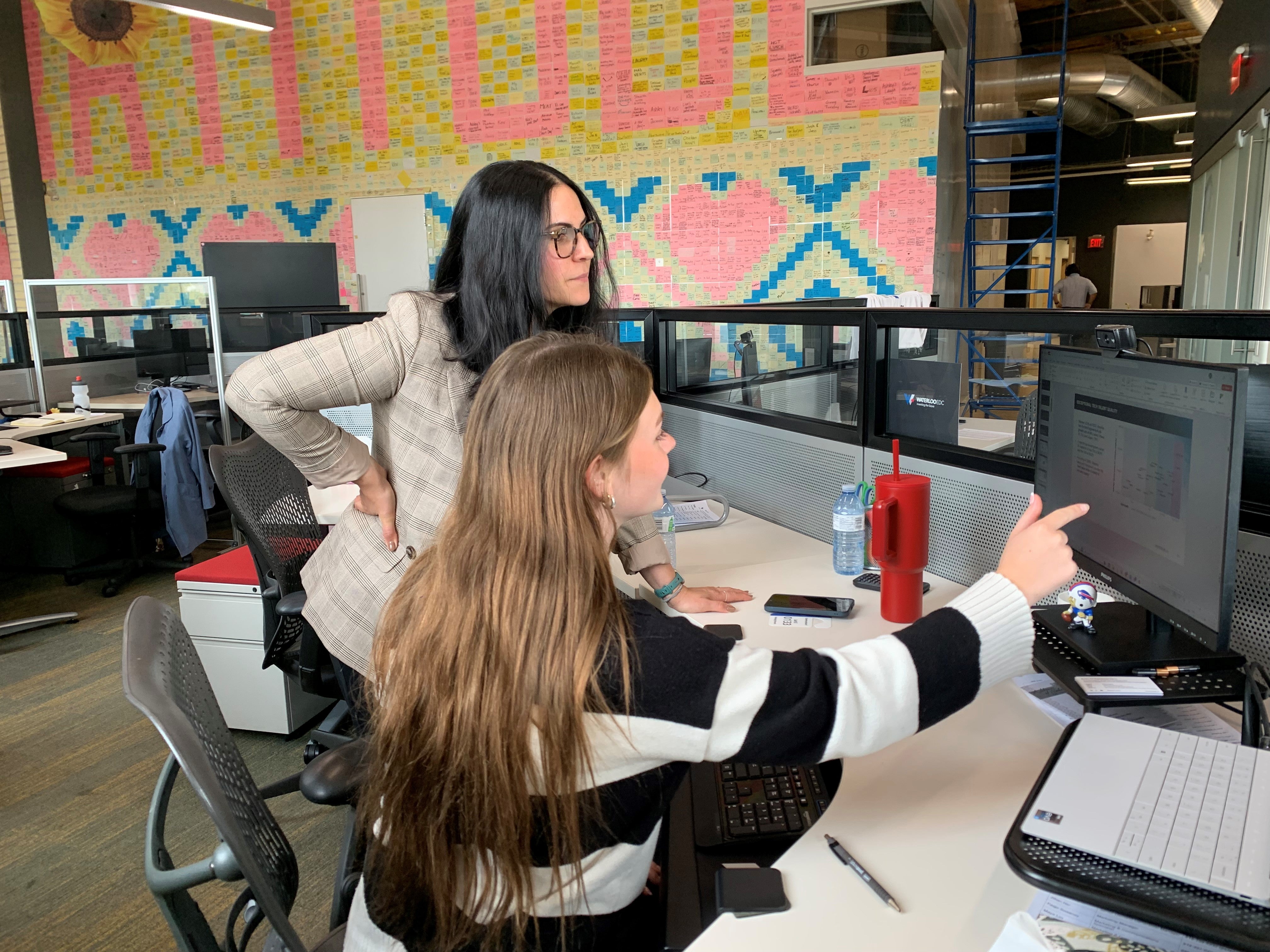 Co-op students points to something on her computer screen while her supervisor looks on. 