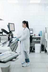 woman standing at a computer desk wearing lab coat