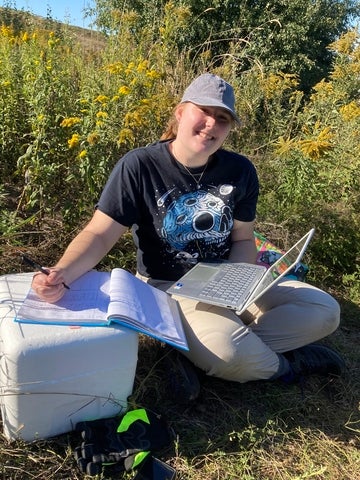 Allison Szenasi in the field holding a laptop by a cooler
