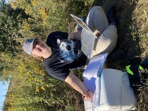 Allison Szenasi in the field holding a laptop by a cooler