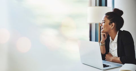 Female employee in office with a laptop looking out window.