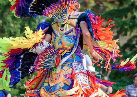 An Indigenous dancer in motion wearing bright coloured Indigenous dance regalia