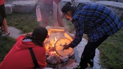 Two students heating their traditional drums in an outdoor fire
