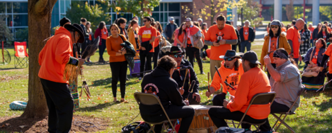Campus Community members dressed in orange shirts gathered outside watching a drum circle