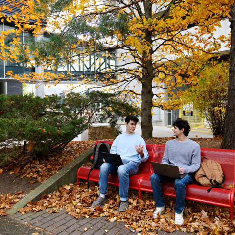 Two Indigenous students in conversation on a red bench outside.