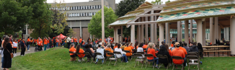 a crowd of people wearing orange shirts sitting outside an outdoor gathering space