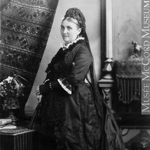 19th-century portrait of Annie McDermot Bannatyne in a dark Victorian dress, posed beside a table.