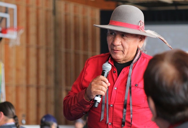 an elder man with a microphone, speaking to an audience