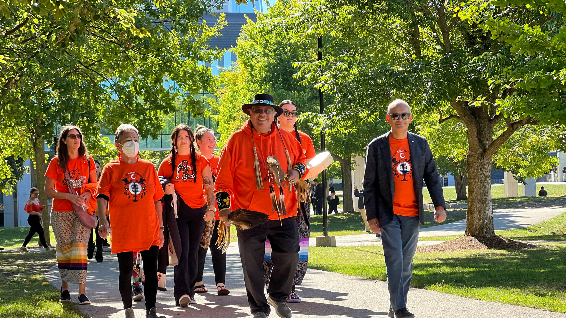 Elder Henry walking with Vivek Goel and others wearing orange shirts