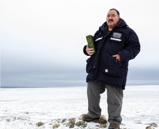 Person in dark blue winter jacket and gray pants standing on snowy terrain, holding a green object