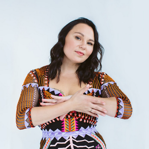 Person with dark hair in a colorful geometric-patterned dress, arms crossed