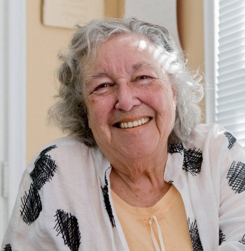 Elderly person with gray hair wearing a patterned shirt and yellow top