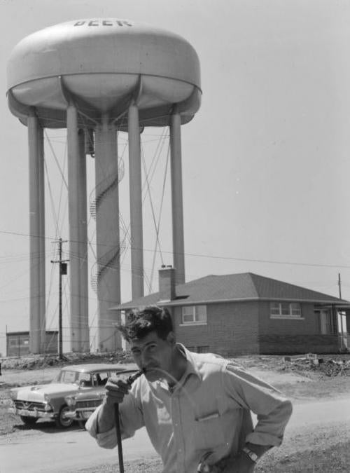 A man drinks from a hose in front of the Lester Street Water Tower with the word 