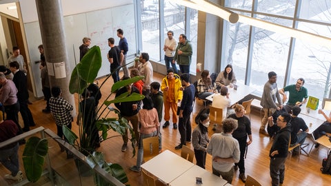 Looking down from a floor above at a large group of IQC community members mingling in the open space near the QNC kitchen