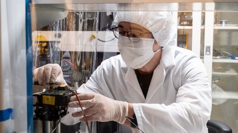 Researcher inside a temporary clean room, adjusting a satellite component