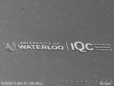Electron microscope close up of the University of Waterloo and Institute for Quantum Computing logos etched into the surface of a diamond