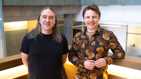 A man in a black shirt and a man in an orange floral shirt standing in a staircase