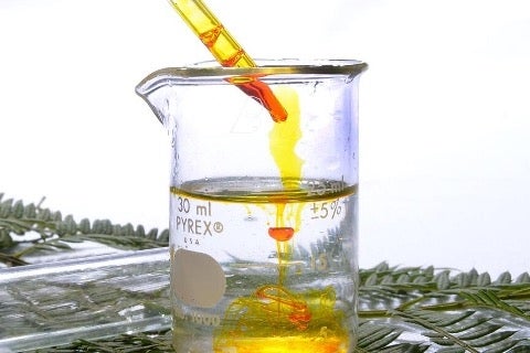 An eyedropper adding orange liquid into a beaker filled with clear, colourless liquid