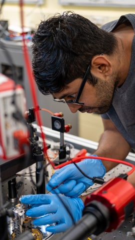 Man wearing blue gloves concentrating on quantum lab equipment