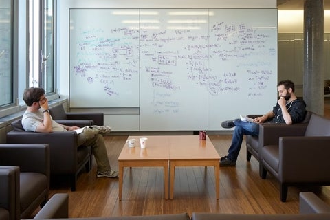 Two male IQC students discussing their ideas in front of a white board covered with equations