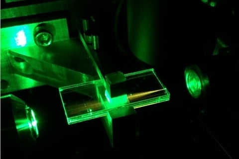 A glass waveguide chip directing green laser light through it