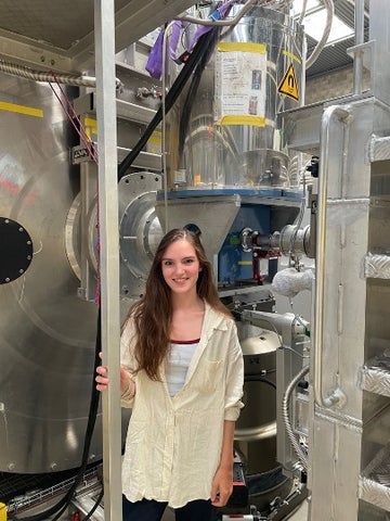 Melissa Henderson standing in front of a large silver scientific instrument filling the room