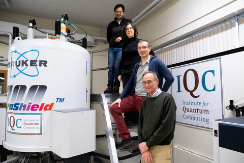 Raymond Laflamme, Eduardo Martín-Martínez, Nayeli Rodríguez-Briones and Hemant Katiyar standing beside an NMR spectrometer