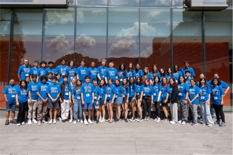 QSYS 2023 group photo, showing close to 50 students in blue t-shirts outside, in front of the QNC building