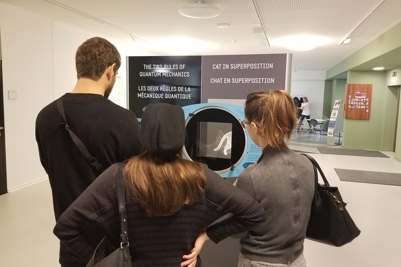 Three standing people look at a panel from QUANTUM: The Pop-Up Exhibition.