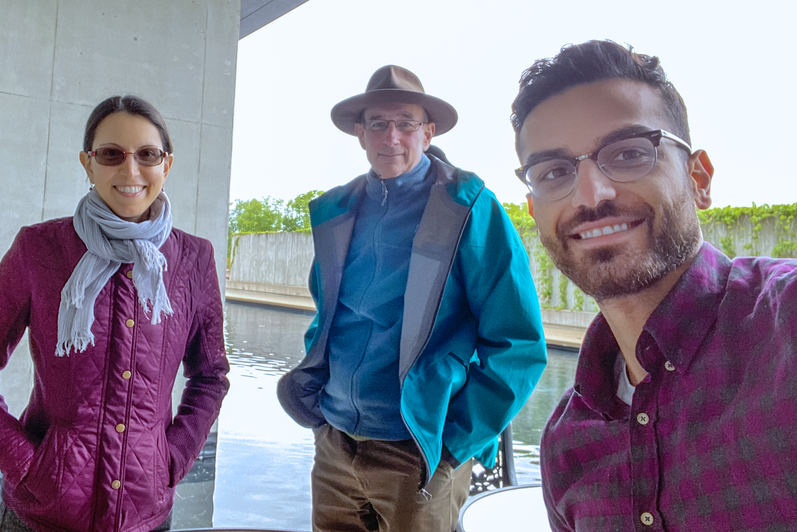 Three people standing outside in front of a pond