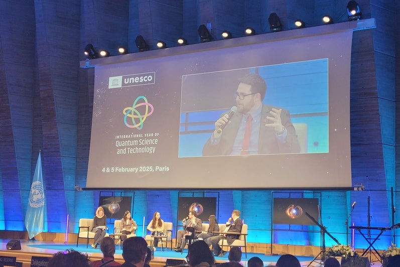 A panel with four people talking in front of a crowd with a projected image of John Donohue in the background