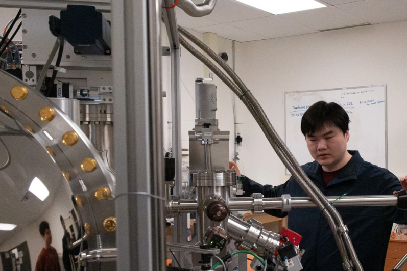 Yawen Peng stands in front of a quantum science instrument 
