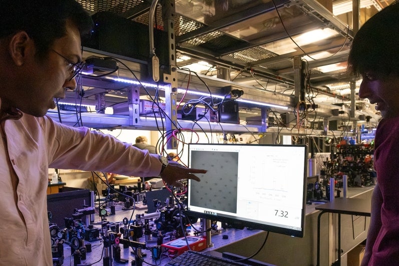 A man points at a computer screen showing dots on the screen with another man looking at the screen as well