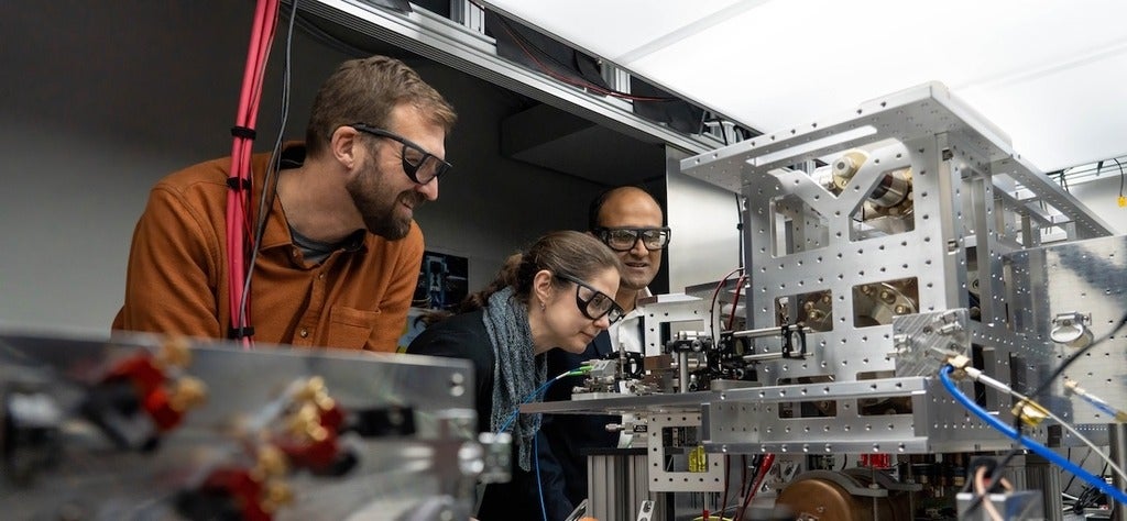 Roger Melko, Crystal Senko and Rajibul Islam (L-R) in a quantum technology lab looking at an ion trap quantum computer