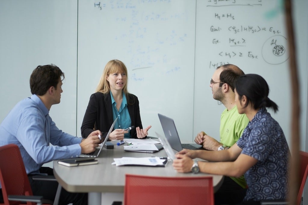Christine Muschik sits at a table with three people looking at her in conversation