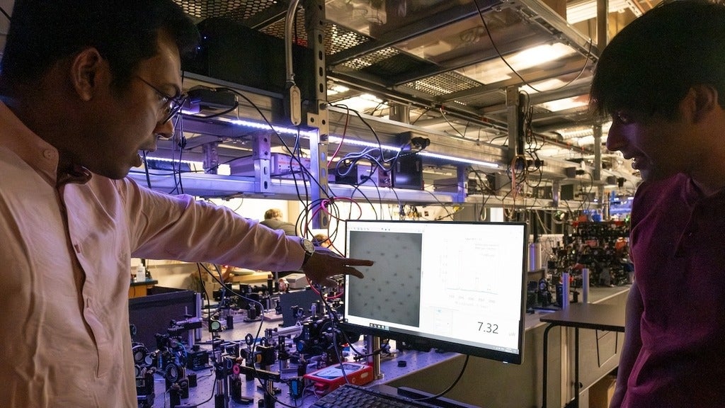 A man on the left pointing at a computer screen that has dots on it and a man on the left looks at the scren