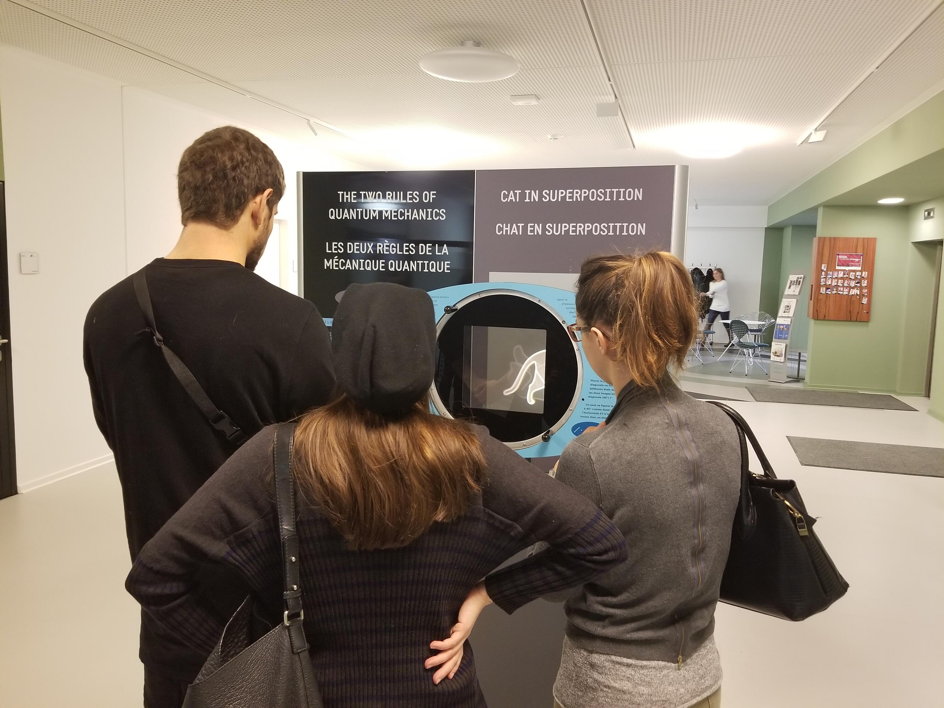 Three standing people look at a panel from QUANTUM: The Pop-Up Exhibition.