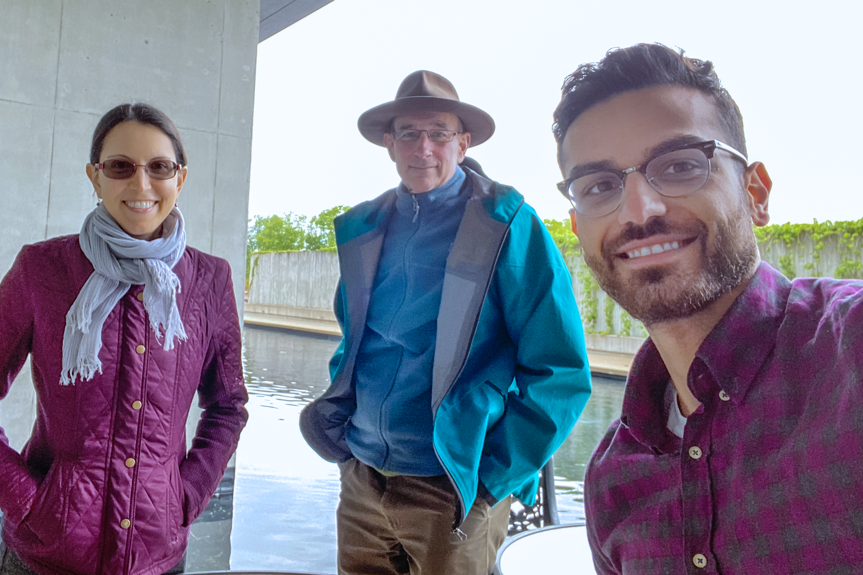 Three people standing outside in front of a pond